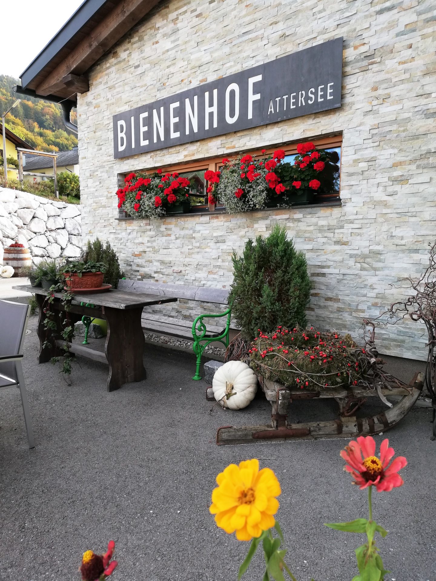 Fassade des Bienenhofs Attersee, mit Blumen geschmückt und einer Sitzbank mit Tisch im Vordergrund