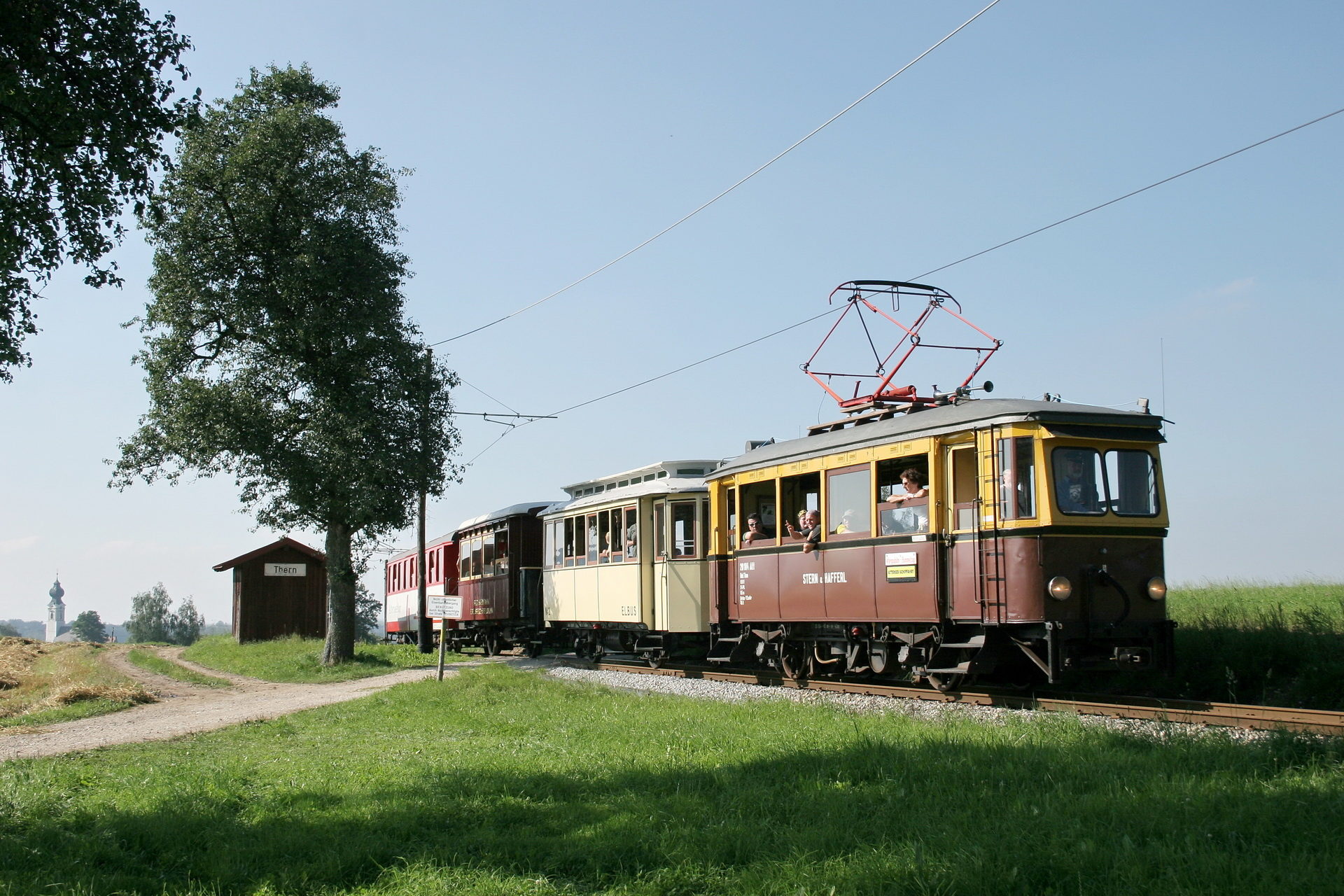 Die historischen Triebwagen der Atterseebahn auf der Strecke, rundherum Wiesen und Felder
