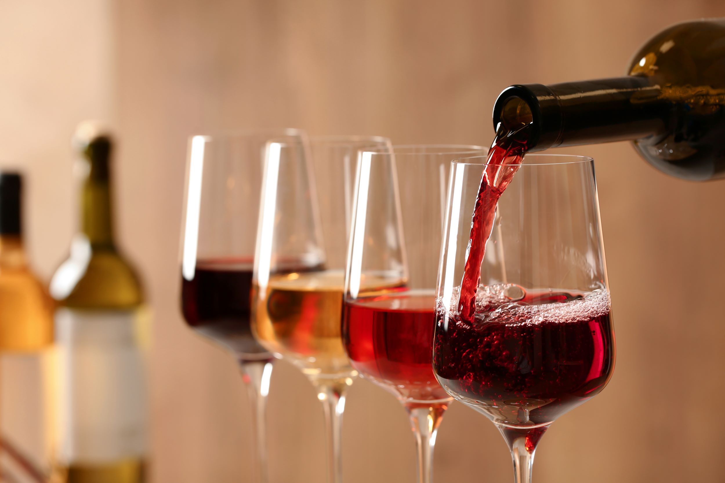 verschiedenfarbige Weingläser, im vordersten wird ein Rotwein eingeschenkt