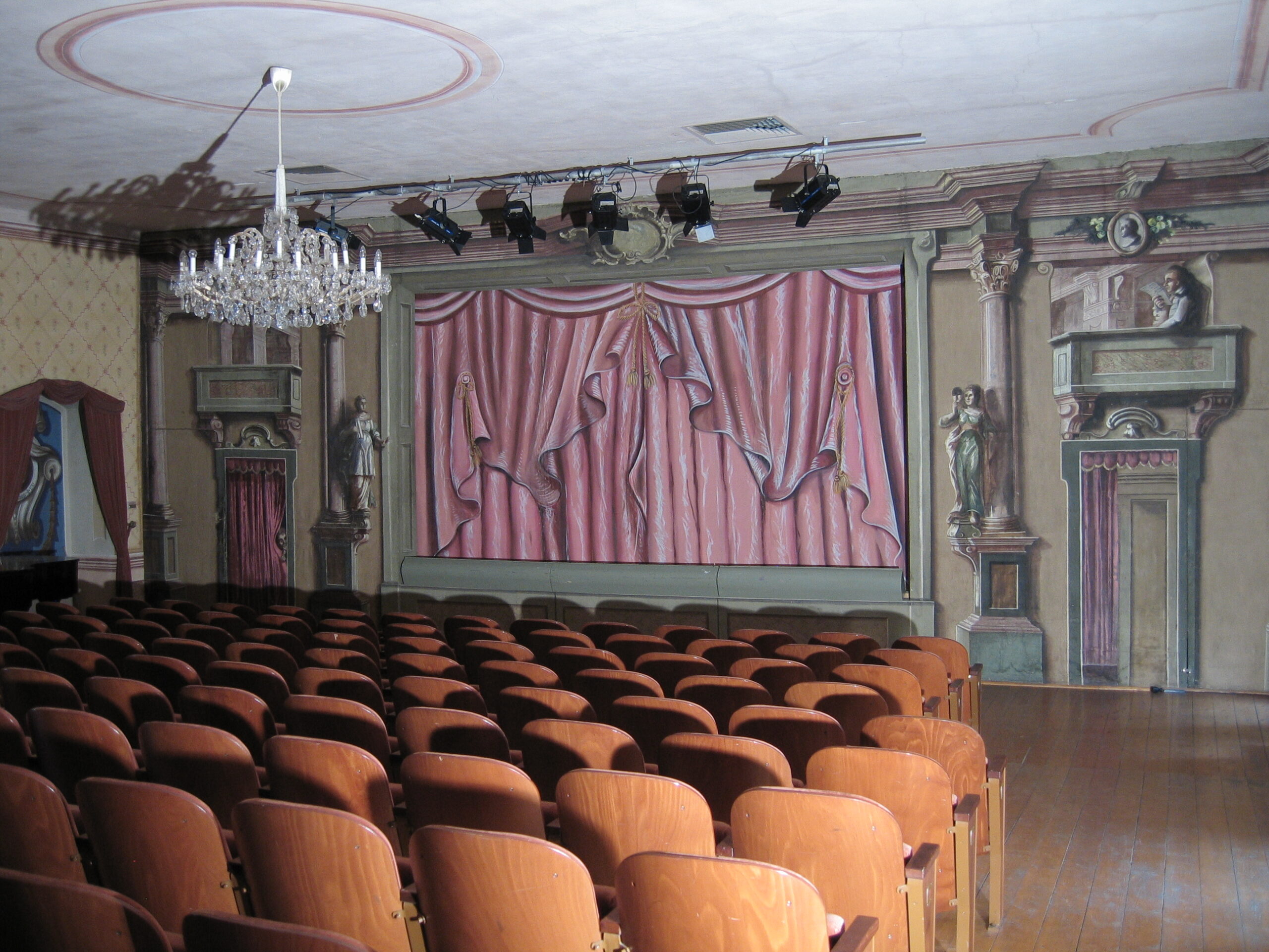 Barocktheater im Stift Lambach, mit Stühlen, einer antiken Bühne, altem Deckenleuchter und Scheinwerfern